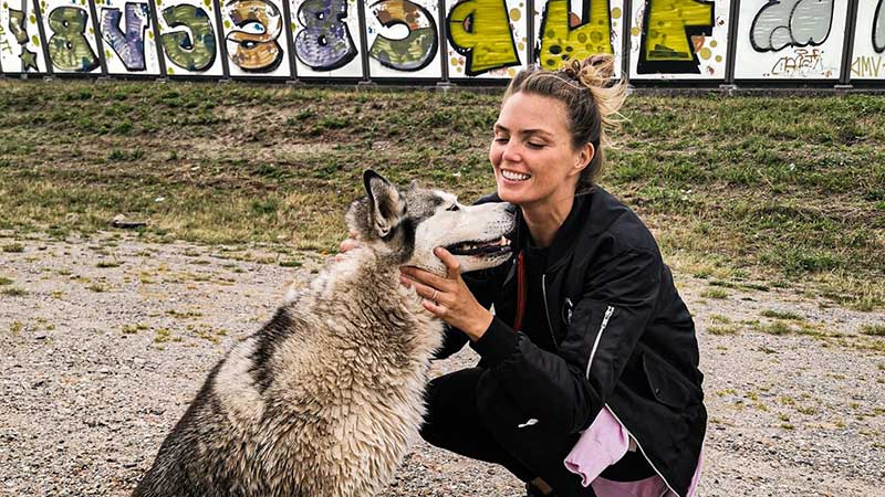 Kim Feenstra knuffelt met hond Micky buiten naast een geluidswal van een grote weg